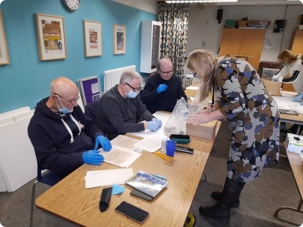 people seated at a table are wearing gloves and handling pieces of medieval pottery.