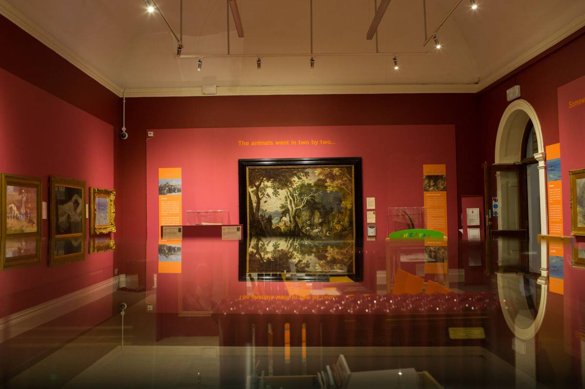 museum gallery room with deep pink walls and a high white ceiling.  The walls are covered in oil paintings.